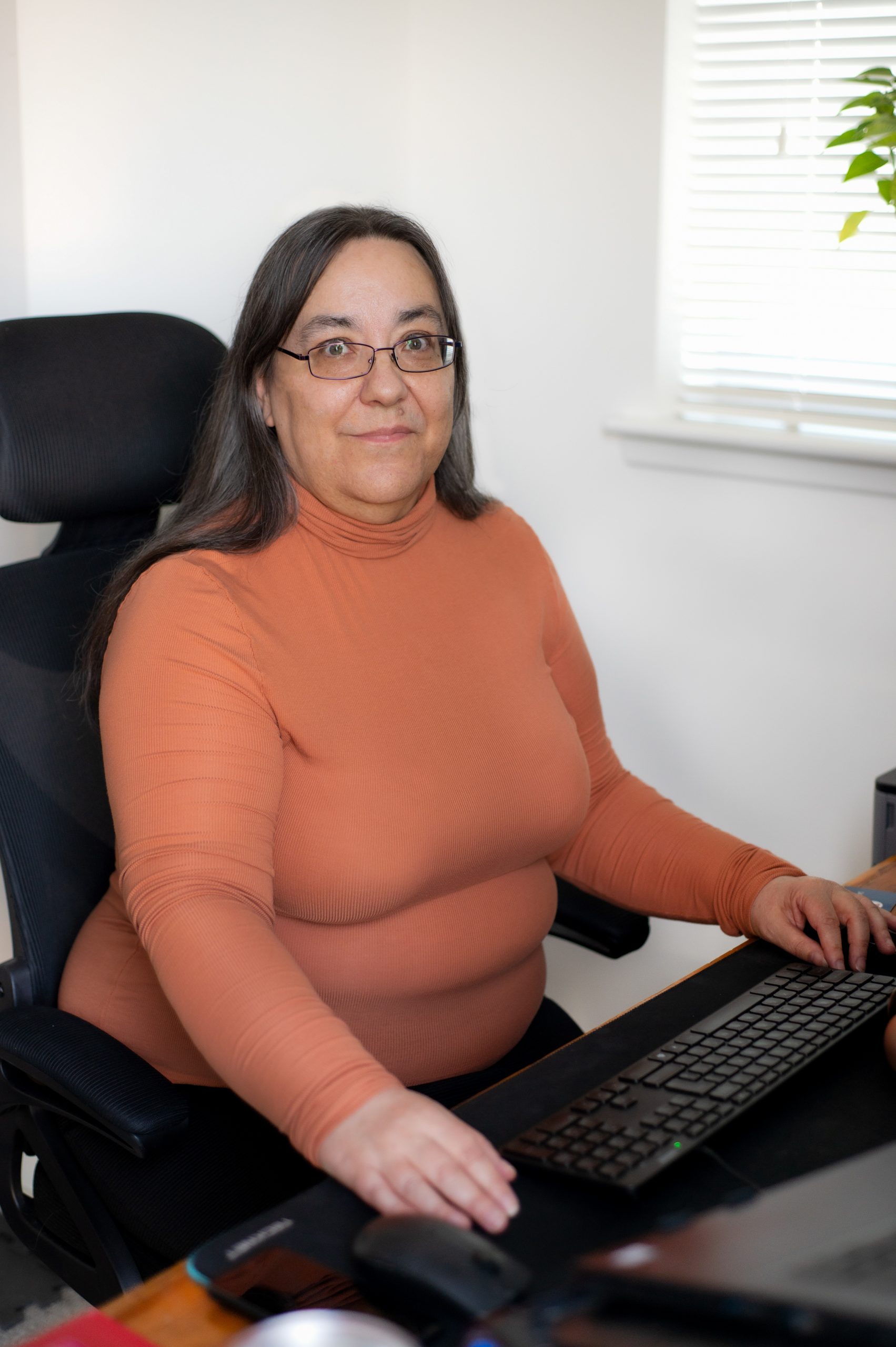 Woman sitting at a desk.  In front of her is a computer keyboard